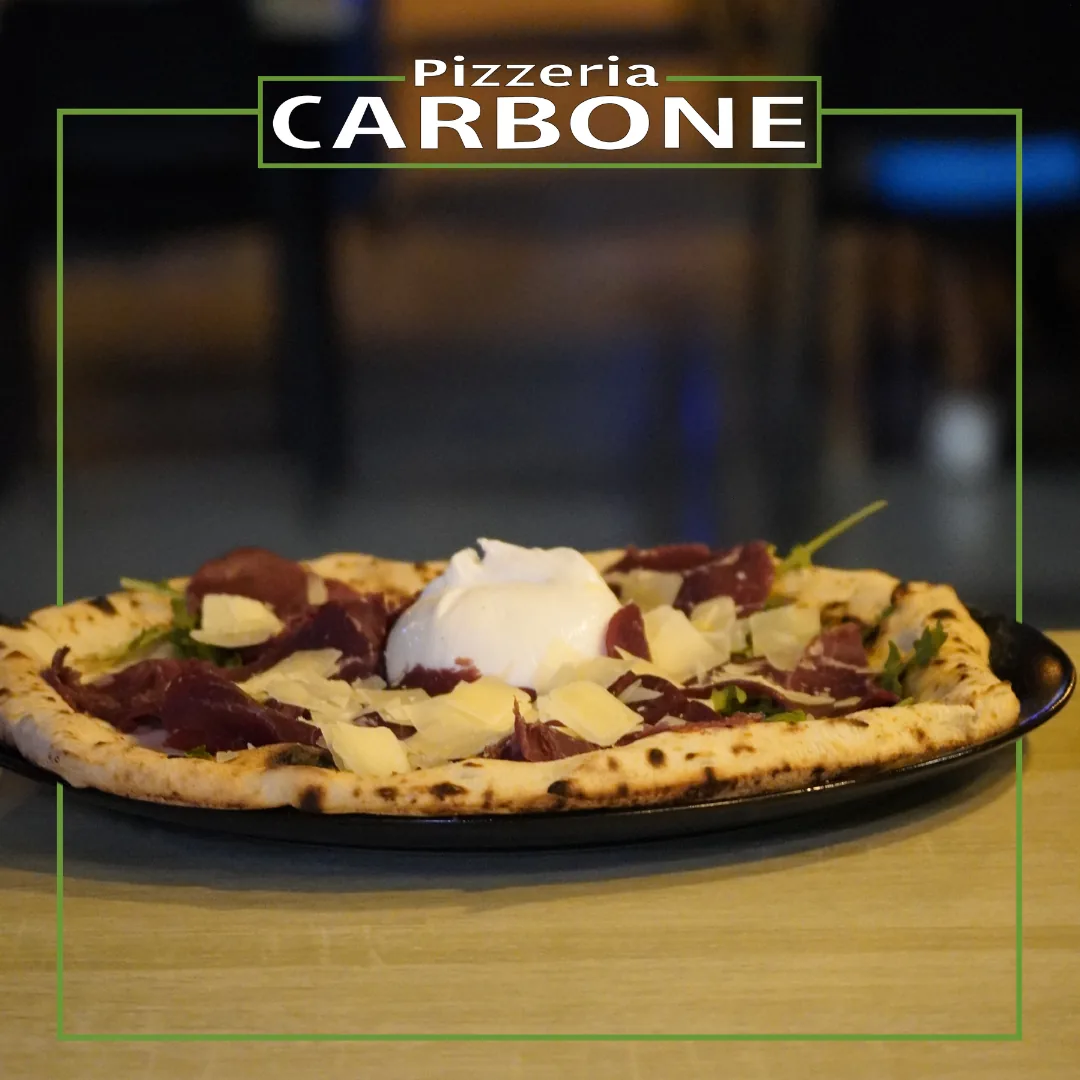 Artisan pizza with cured meat and fresh cheese, served on a black plate