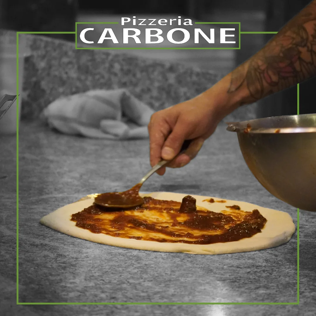 The pizzaiolo’s hands spreading sauce across the dough