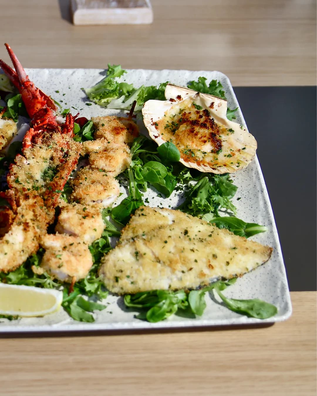 Tray of oven-baked fish and scallops on a bed of greens with lemon
